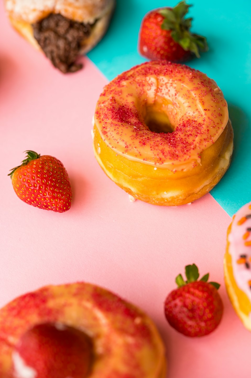 Donuts and fresh strawberries arranged on a bright pink and turquoise background.
