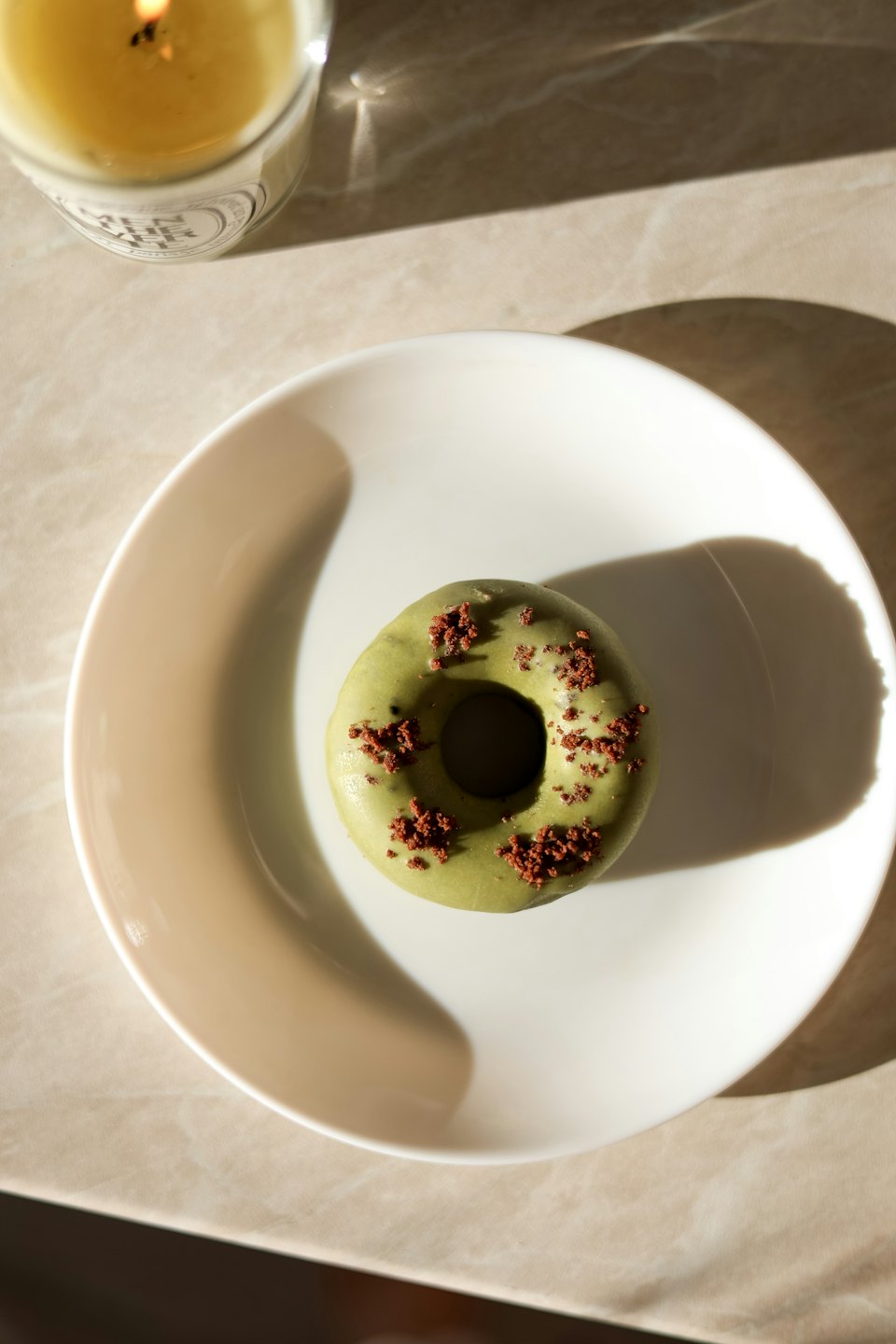 A matcha glazed donut sits on a white ceramic plate.