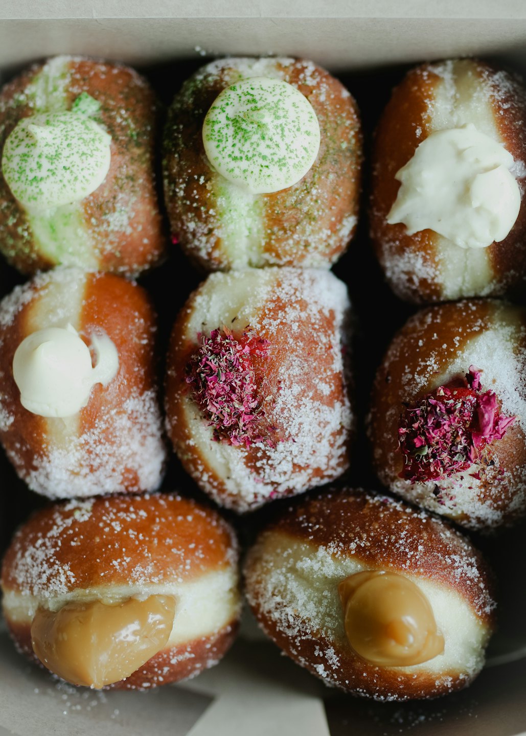 Nine donuts with various toppings in a cardboard box.