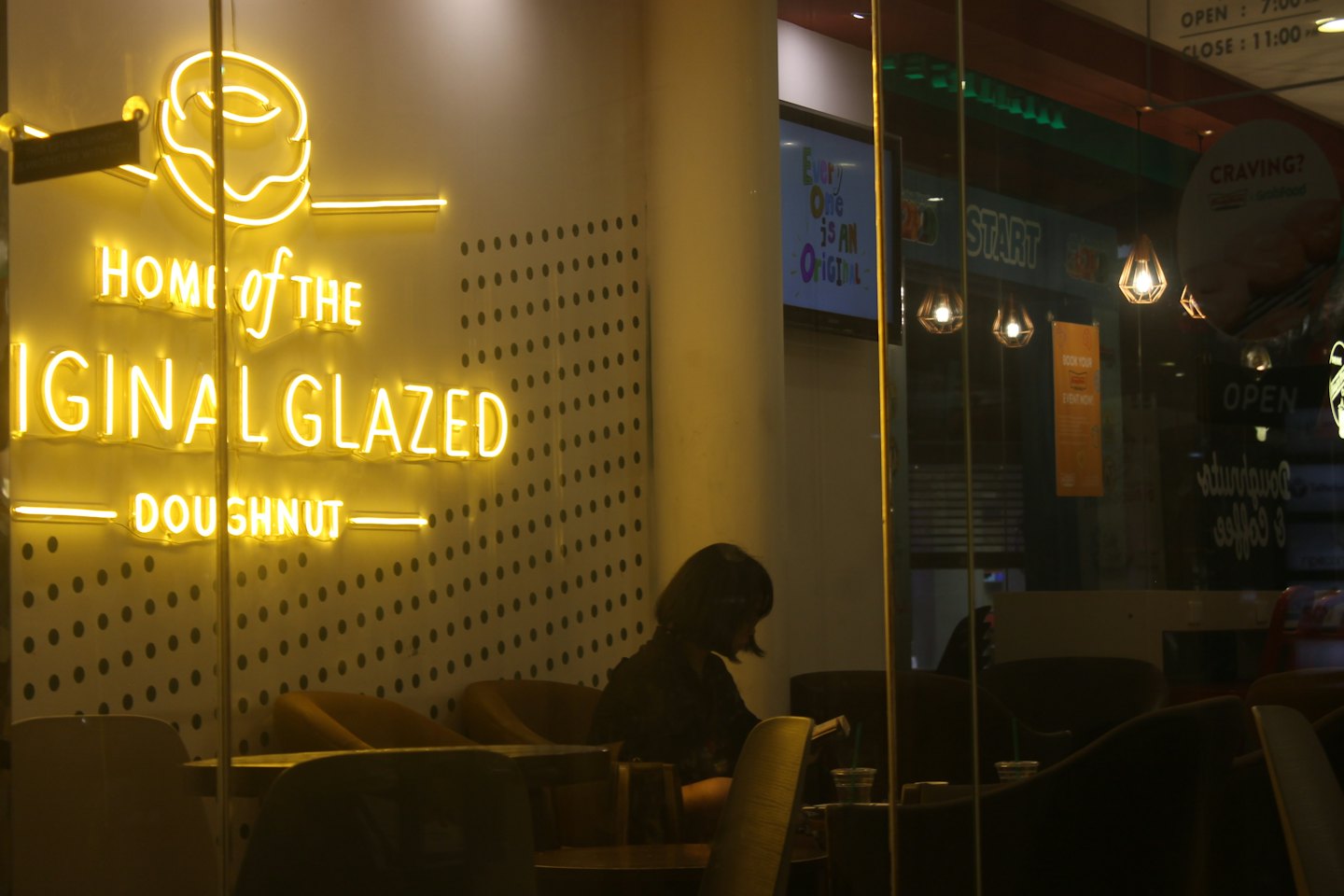A person reads at a table inside a donut shop.