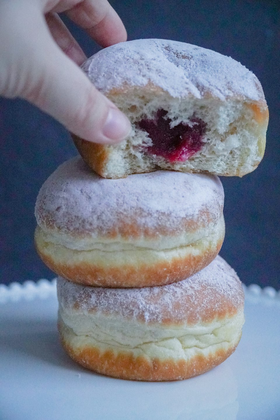 Hand holding a powdered sugar donut with visible red jam filling.