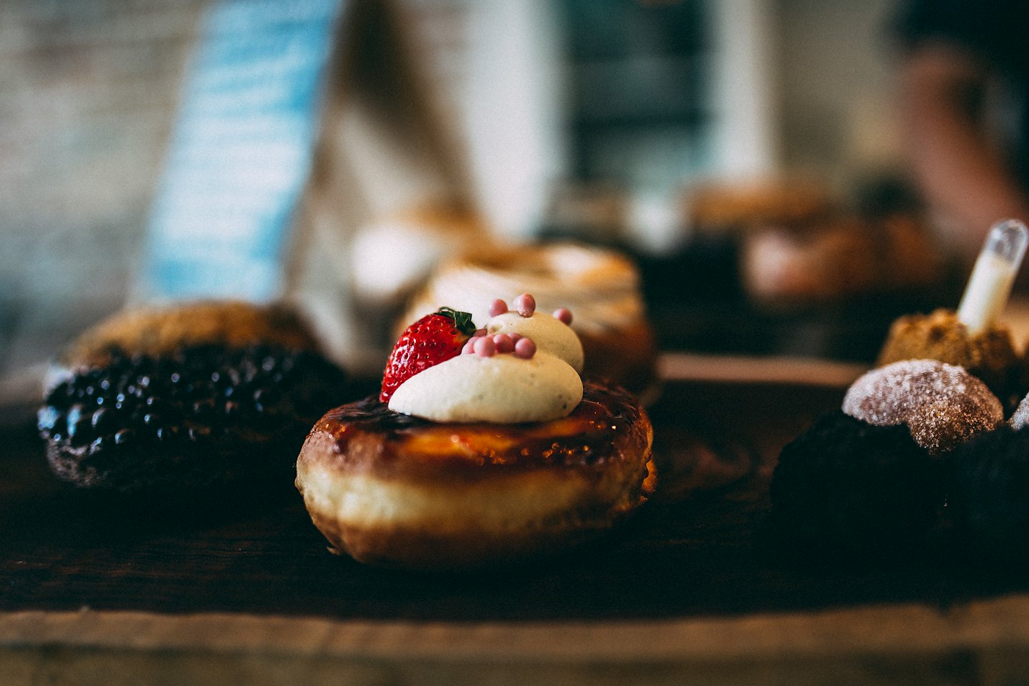 Glazed donut with whipped cream, sprinkles, and strawberry on wood.