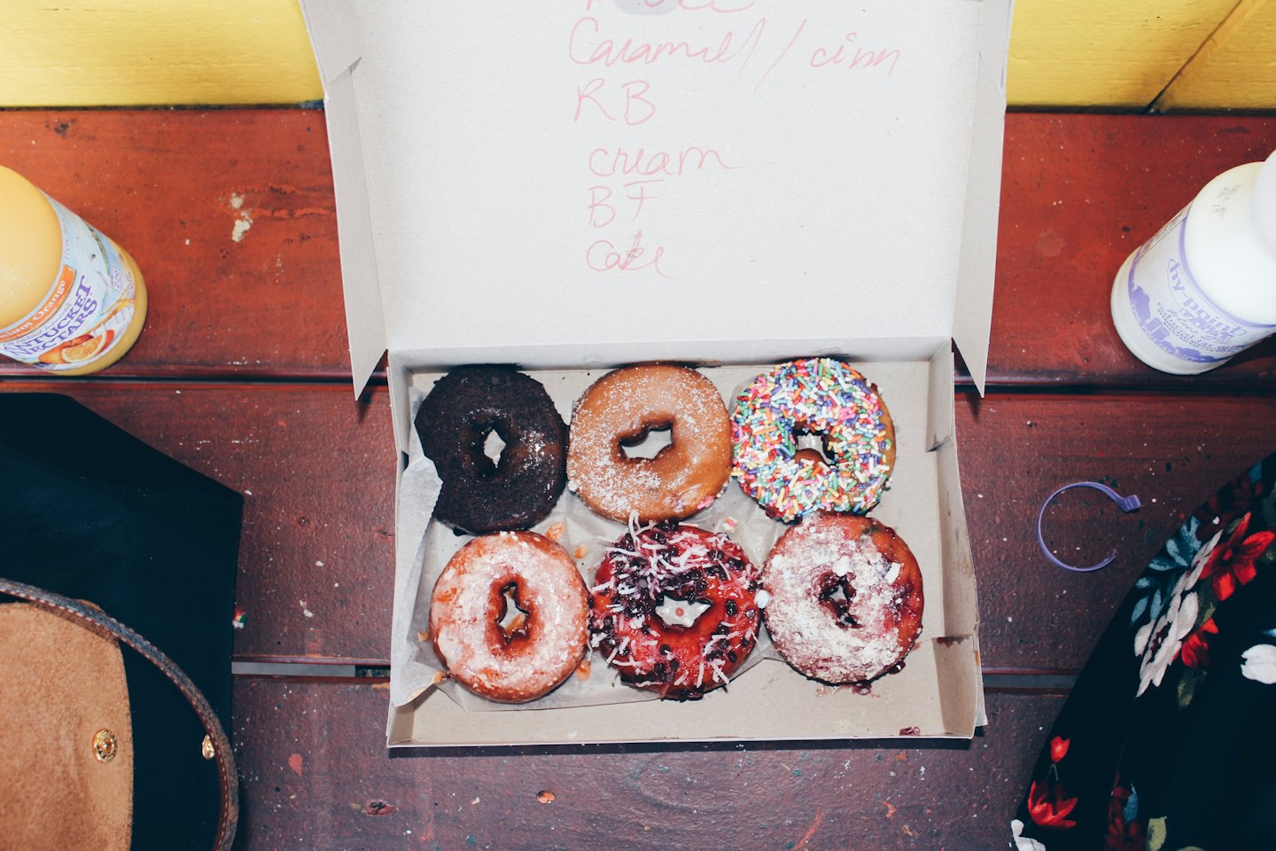 Six assorted donuts inside a cardboard box on a rustic table.